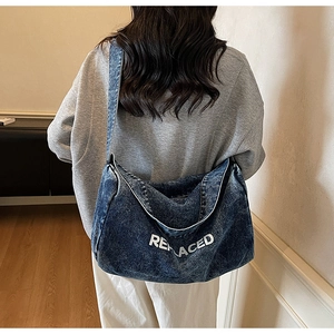 Detail of large denim tote bag featuring white REPLACED embroidery and street style texture