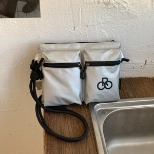 Detail of silver nylon crossbody bag with dual zip pockets and knotted rope strap
