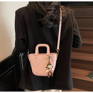 Petit sac seau rose avec détails dorés et breloque porté par un mannequin