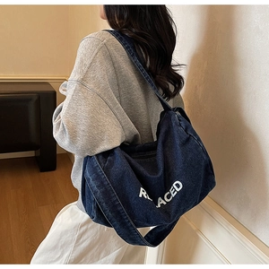 Denim tote bag with REPLACED print worn by a model in a minimalist indoor setting