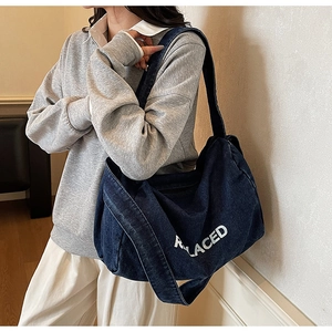 Detail view of large denim tote bag featuring white letter printing and casual shoulder strap