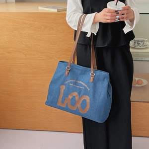 Detailed close-up of blue denim tote bag with brown leather straps and printed text