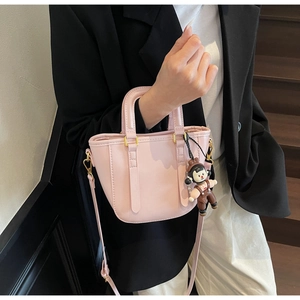 Détail d'un sac seau rose avec ferrures dorées et un pendentif de dessin animé sur l'anse