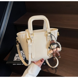 Détail d'un sac seau blanc cassé avec breloque de poupée en perles sur escalier