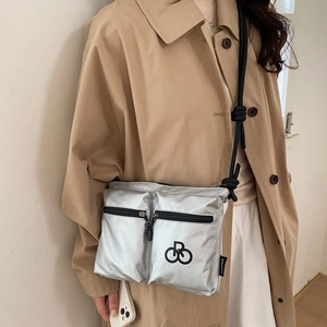 Close-up of metallic silver nylon crossbody bag with zipper pockets and logo on a beige coat