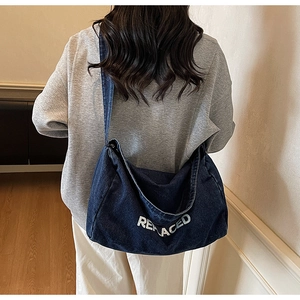 Detailed back view of a dark blue denim tote bag with REPLACED text on a model