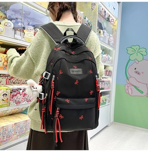 Dettaglio zaino nero in nylon con ricami a fiocco rosso e tiranti della zip intrecciati