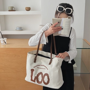 Detail of a large off-white canvas tote bag with brown handles and elegant printed slogans