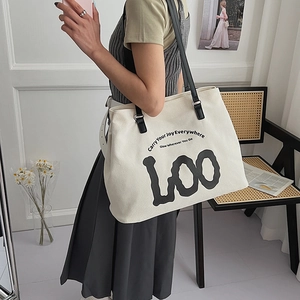 Close-up of beige canvas tote bag featuring black letter print and thin leather straps