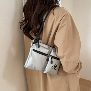 Silver nylon crossbody bag with black rope strap shown on model over khaki trench coat