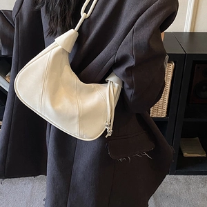 Detail view of cream-colored shoulder bag featuring knot handle and silver ball charm
