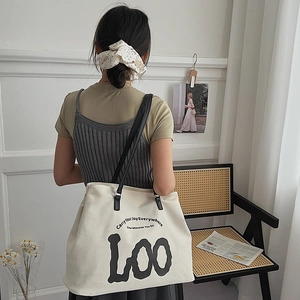 Detail view of a white canvas tote bag with black LOO lettering and large capacity