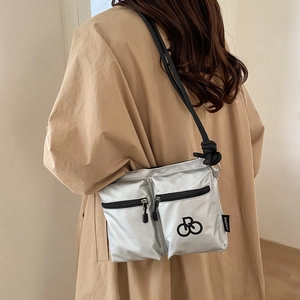 Detail of silver reflective nylon crossbody bag with dual front zippers and rope strap