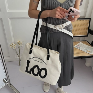 Detail of white canvas tote bag with black leather handles and modern text print