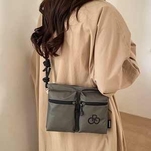 Detail of gray-green nylon crossbody bag with multi-zipper pockets and rope strap