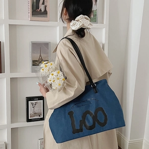 Detailed view of dark blue denim tote bag with black LOO artistic text and leather strap