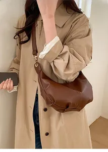 Detail of a brown pleated hobo shoulder bag with gold hardware worn with a beige trench coat
