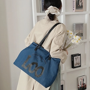 Detailed shot of a blue denim tote bag with black leather straps and Joy typography