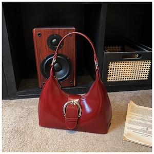 Detail shot of a dark red patent leather crescent bag with a large silver round buckle