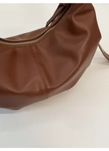 Detailed close-up of brown leather texture and stitching with gold zipper on crossbody bag