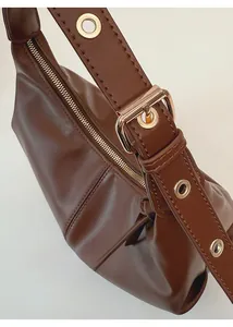 Detail of adjustable shoulder strap with gold-tone buckle on tan leather dumpling bag
