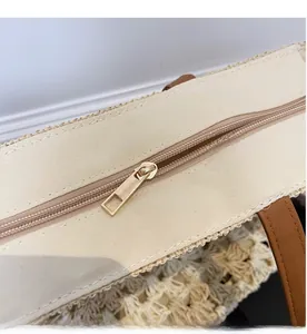 Detailed close-up of smooth gold metal zipper and beige canvas trim on a straw tote bag