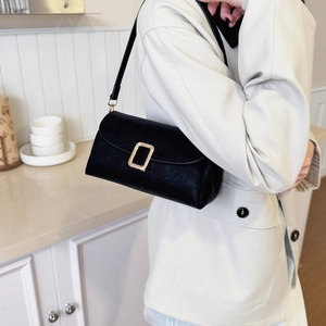 Dettaglio dell'elegante borsa a tracolla in camoscio nero con fibbia dorata indossata dal modello