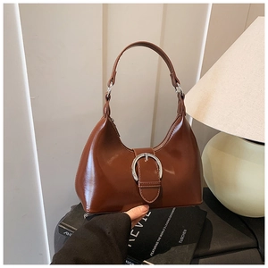 Detailed shot of caramel crescent bag with glossy finish and silver buckle on books