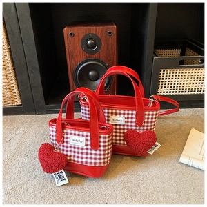 Vista detallada de bolsos cubo de cuadros rojos con colgantes de corazón y asas de cuero