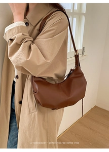 Detailed side view of a minimalist brown croissant shoulder bag styled with a khaki trench coat