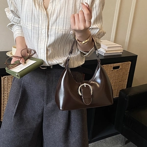 Detail showing deep brown patent leather texture and silver horseshoe buckle on underarm bag