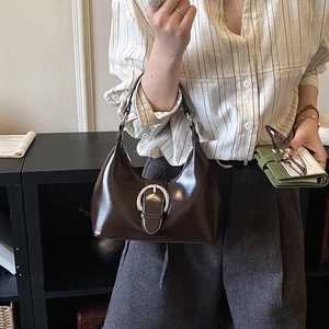 Detail of dark brown patent leather shoulder bag with a large silver horseshoe buckle
