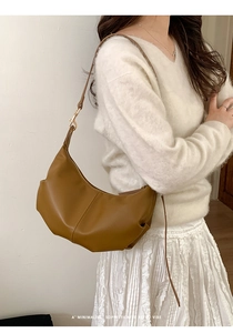 Caramel crescent shoulder bag with gold zipper detail worn by a model in a minimalist setting