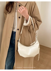 Detail shot of minimalist white leather croissant bag with gold-tone hardware and strap