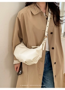 Minimalist cream crescent bag worn crossbody by a model in a beige trench coat