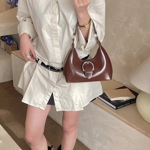 Detail of a brown glossy leather hobo bag with a silver horseshoe buckle and retro strap