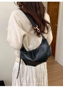 Detail of a black pleated crescent hobo bag with gold metal hooks and shoulder strap