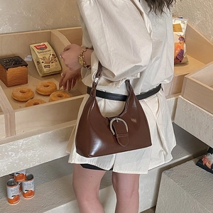 Close-up of brown glossy patent leather underarm bag with silver buckle in cafe setting
