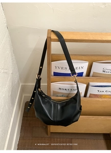 Minimalist black pleated half moon bag hanging on a wooden rack with gold hardware details