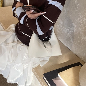 Detail of creamy white patent leather bag with a large silver buckle shown on a model
