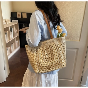 Detail of hand-woven straw tote bag with brown leather straps and floral accents