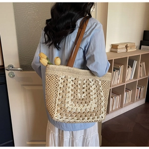 Detail of hand-woven straw tote bag featuring hollow geometric crochet patterns and leather straps