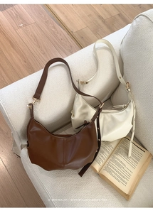 Detail of minimalist pleated hobo bags in brown and beige colors on soft fabric