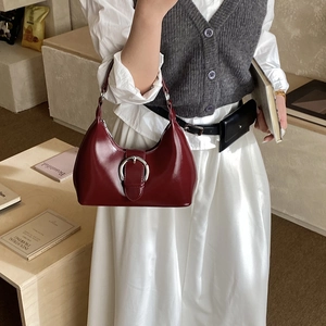 Detail of red patent leather shoulder bag with a large silver round buckle and glossy finish