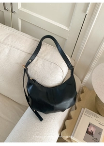 Detail of black crescent hobo bag featuring pleated leather design and gold buckle