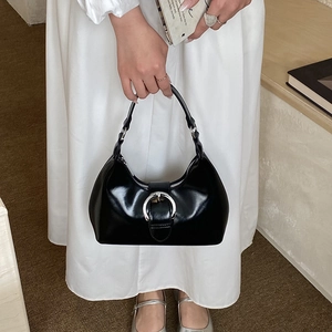 Detail of black glossy handbag with oversized silver metal buckle shown on shoulder