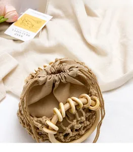 Detail of beige woven bucket bag with round wooden handle and drawstring closure