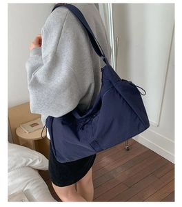 Detail of a large navy nylon crossbody bag showing the side drawstring pocket and zipper