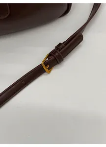 Detailed close-up of dark brown leather bag strap with golden adjustable buckle