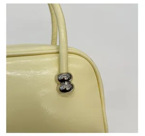 Detailansicht der silbernen Kugelbeschläge und Lederstruktur an einer gelben Handtasche